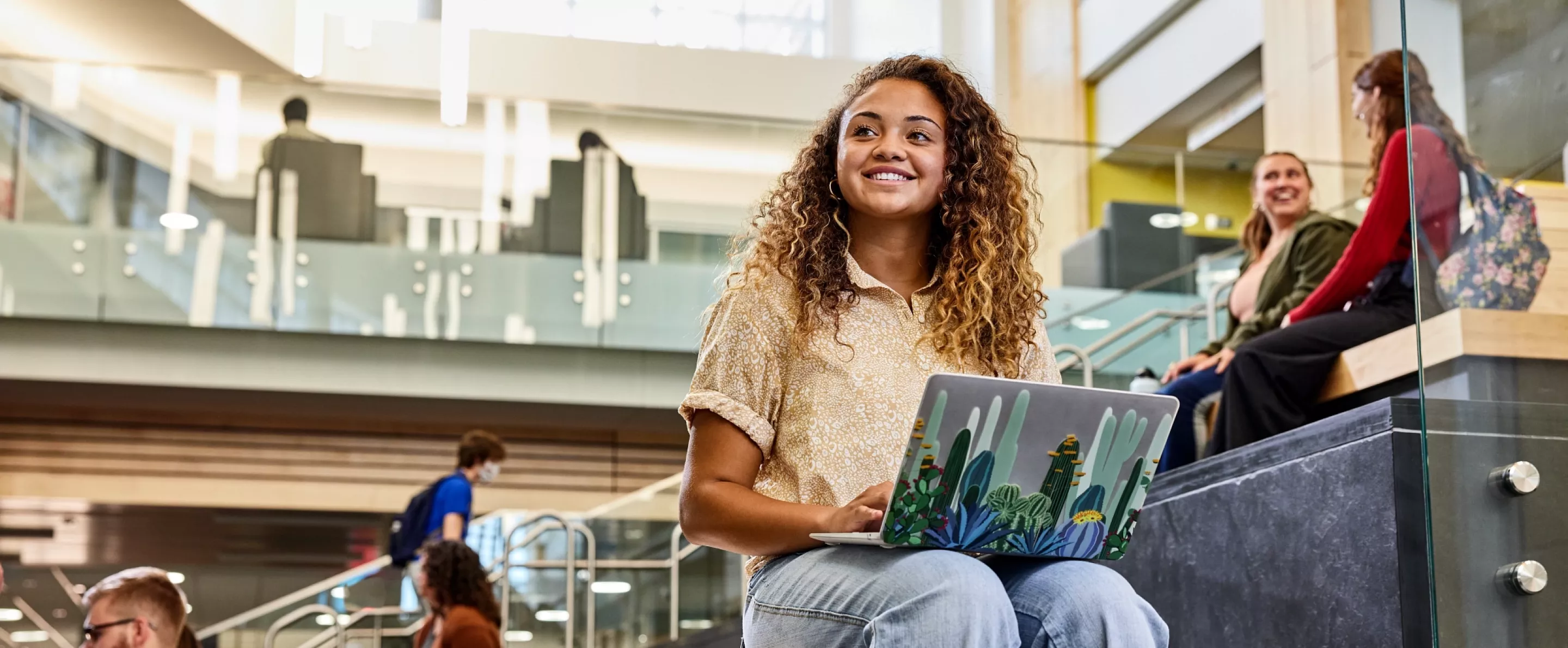 Student recognizes another student walk into the Belknap Academic Building as she is typing on her laptop and sitting on the…