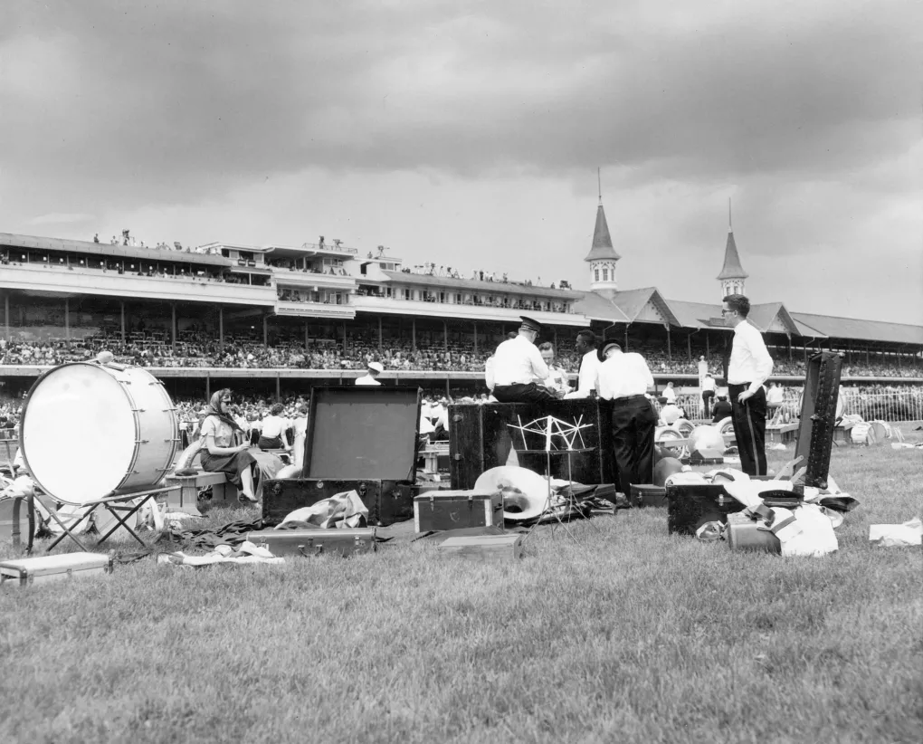 A black and white photo from 1958 of the Cardinal Marching Band setting up on the turf track at Churchill Downs. Twin Spires in the background.