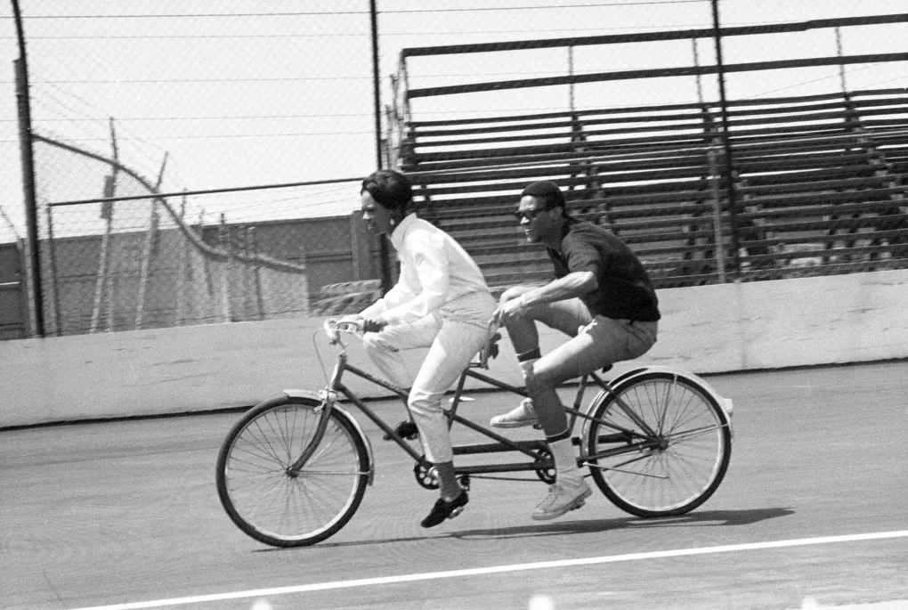 A black and white photo from 1968 of a man and woman racing on a tandem bicycle.