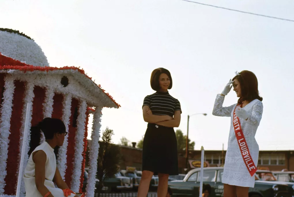 A color photo of three women standing atop a UofL Homecoming parade float in 1968.