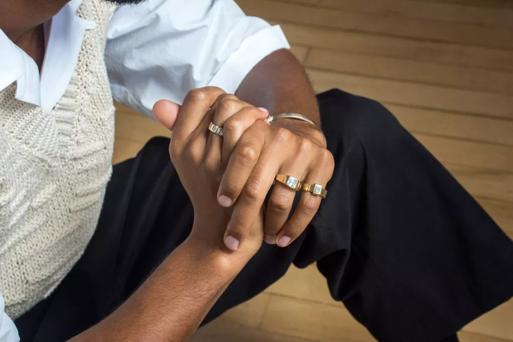 Three golden rings with diamond stones on a woman's clasped hands.