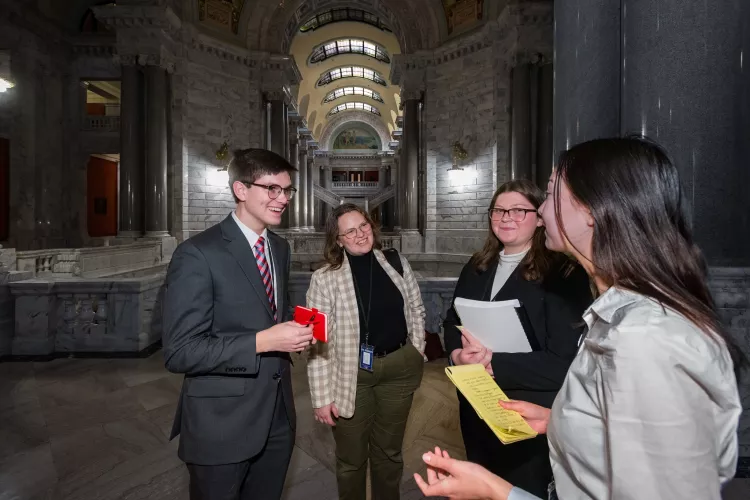 three young women and one young man all dressed professionally gather in a hallway in a government building