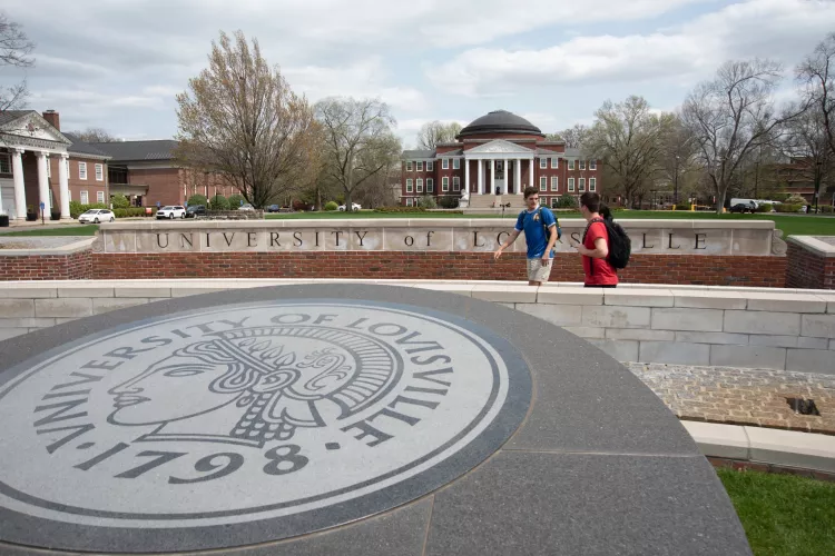 Students walking and talking near the 3rd Street entrance with Grawemeyer Hall and the School of Law buildings in the background