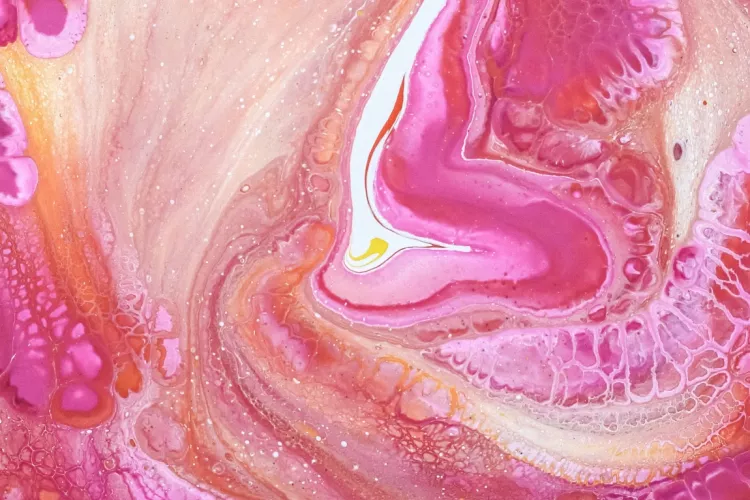 Close-up of the liquid swirls of a pink and yellow fluid painting.