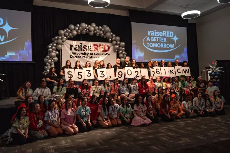 Students hold up white cards that show $533,902.79. Other students stand around cheering.