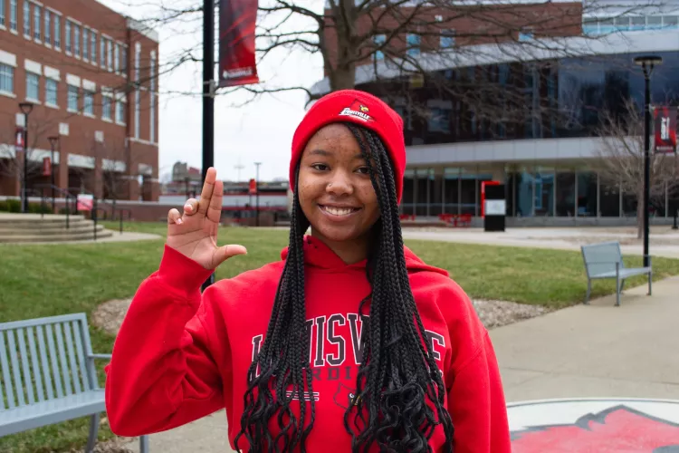 Woman wearing red UofL sweatshirt holding up a "L" sign