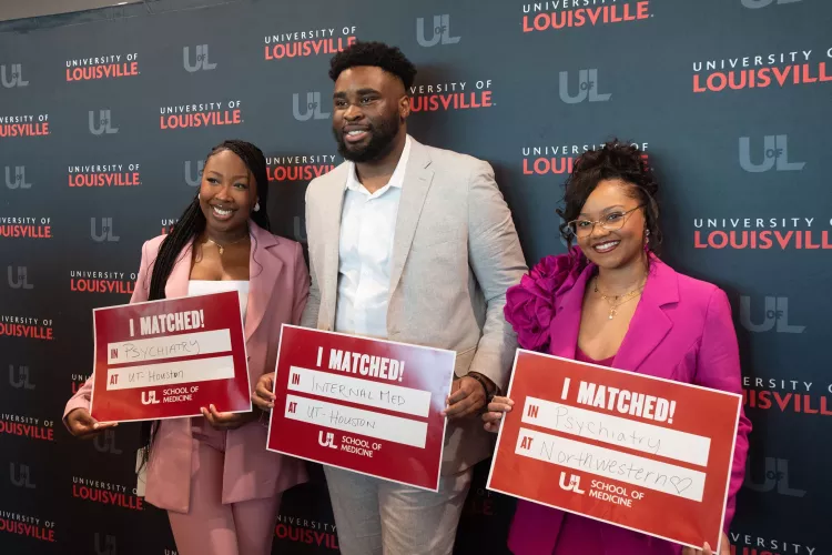 Three medical students hold signs indicating their residency placement.