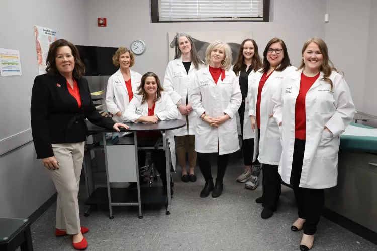 Kentucky Racing Health Services Center (KRHSC) Staff and University of Louisville School of Nursing faculty in an exam room located in the Center. A photo of a horse is behind the members. They are wearing their white lab coats.