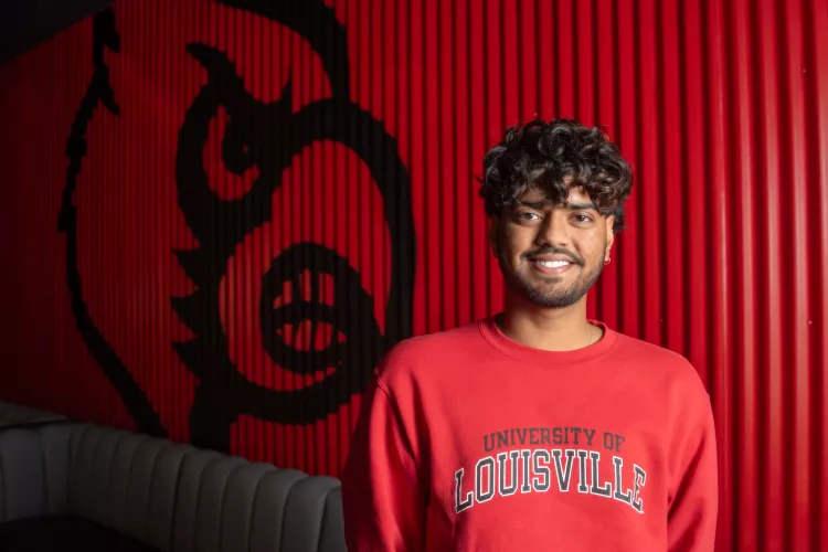 Student in red UofL sweatshirt with Cardinal bird on wall behind him.