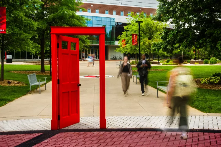 A red doorway on campus with students and an academic building