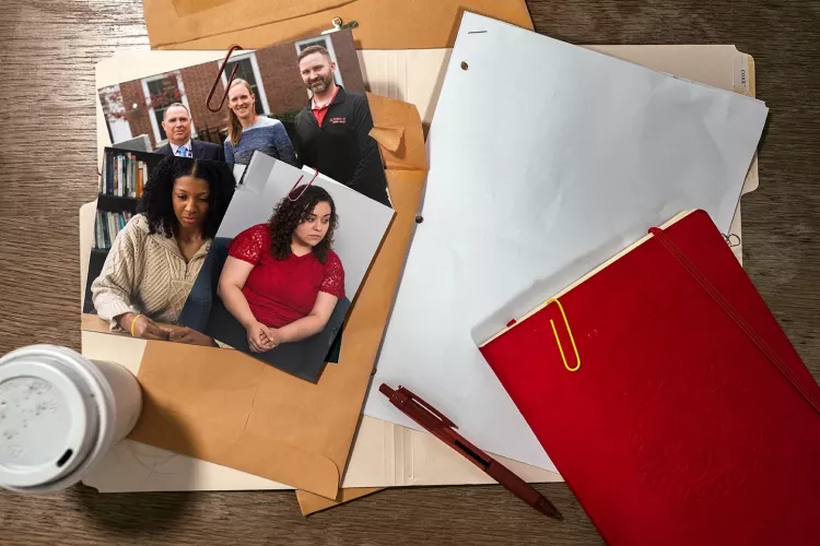 A red notebook and red pen on a desk with folders and photographs.