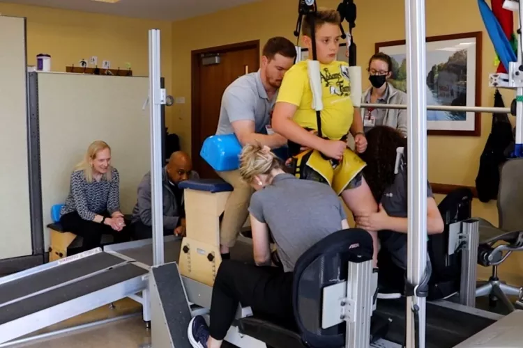 Child on treadmill assisted by trainers