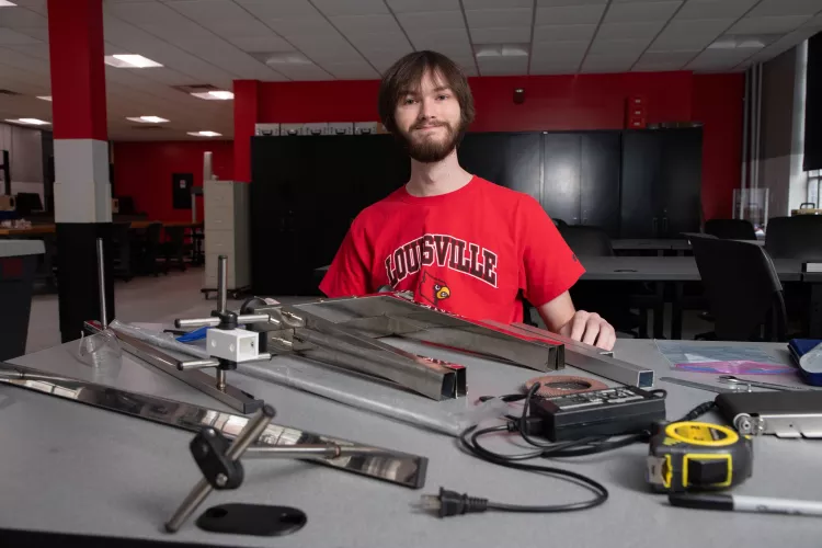 Young man smiling at worktable with metal and electrical parts