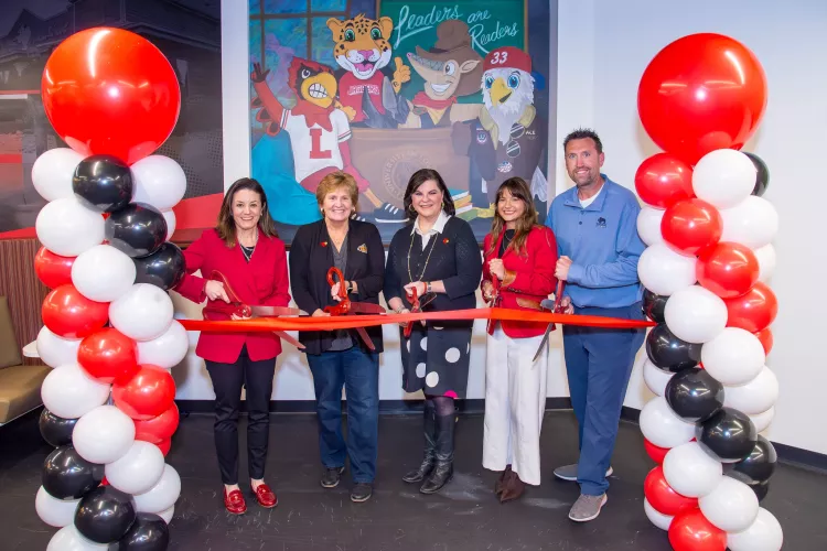 Five people cutting a red ribbon in front of character mural