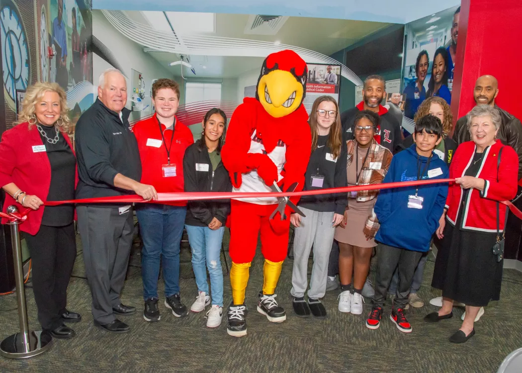 a group of men, women and children join a mascot dressed as a Cardinal to cut a ribbon