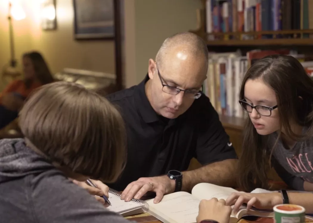 a man is studying at his home with two chilkdren sitting with him at a table