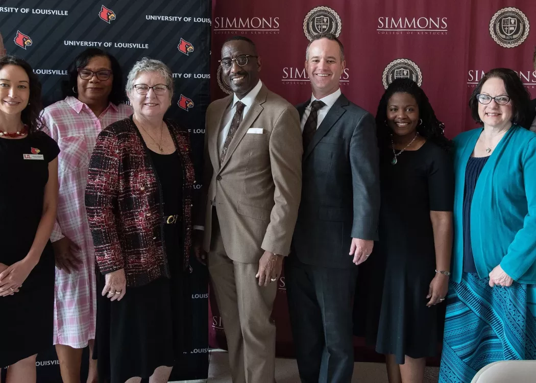 Group of researchers standing in front of UofL and Simmons College backdrops