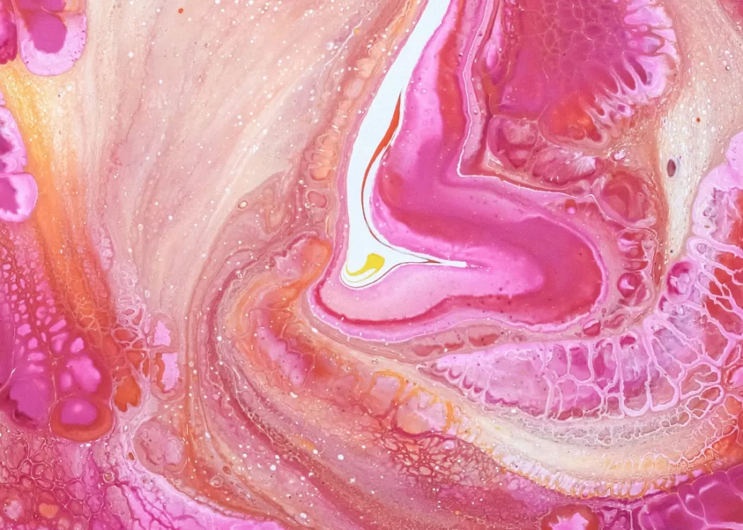 Close-up of the liquid swirls of a pink and yellow fluid painting.