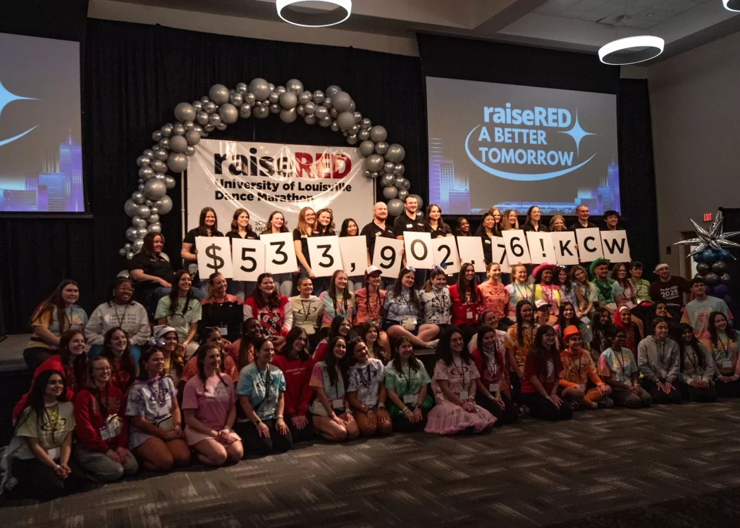 Students hold up white cards that show $533,902.79. Other students stand around cheering.