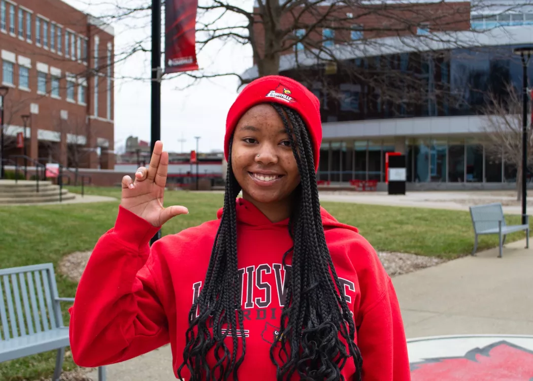 Woman wearing red UofL sweatshirt holding up a "L" sign