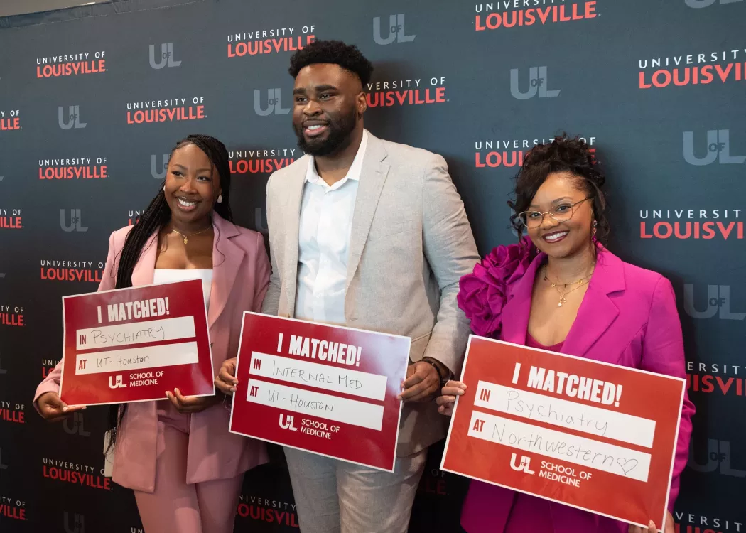 Three medical students hold signs indicating their residency placement.