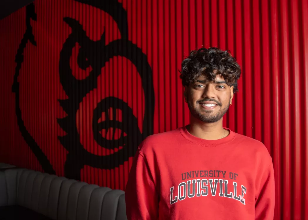 Student in red UofL sweatshirt with Cardinal bird on wall behind him.
