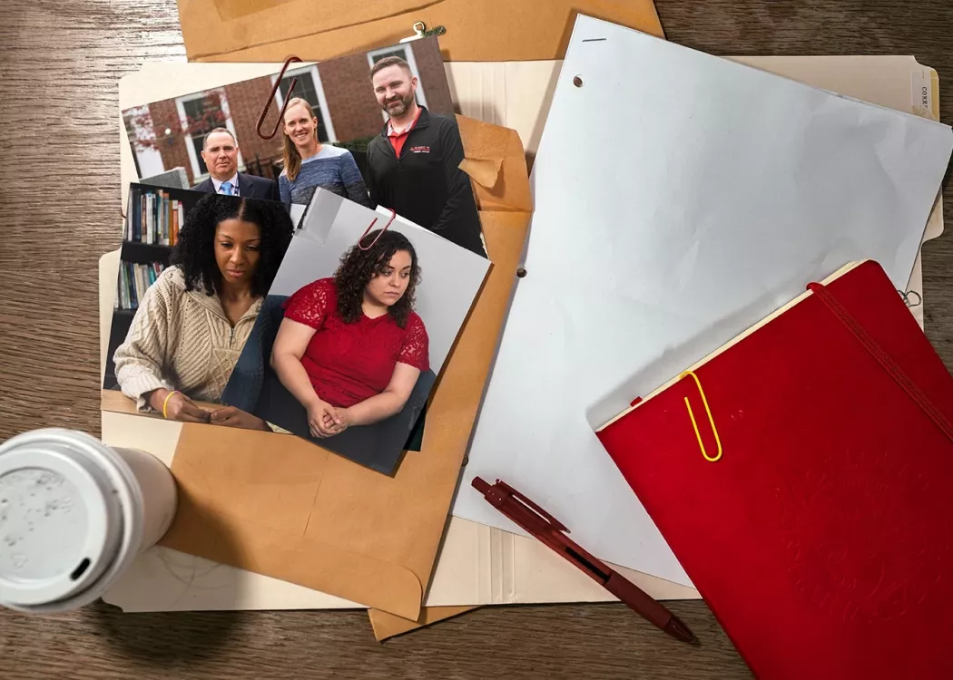 A red notebook and red pen on a desk with folders and photographs.