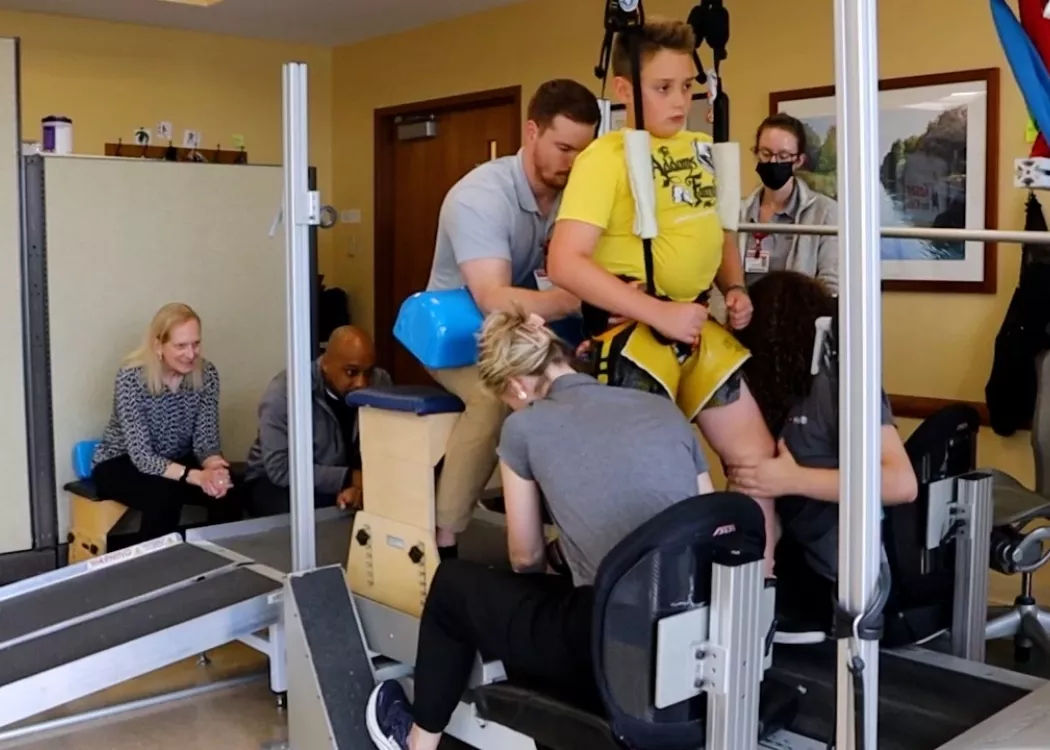 Child on treadmill assisted by trainers