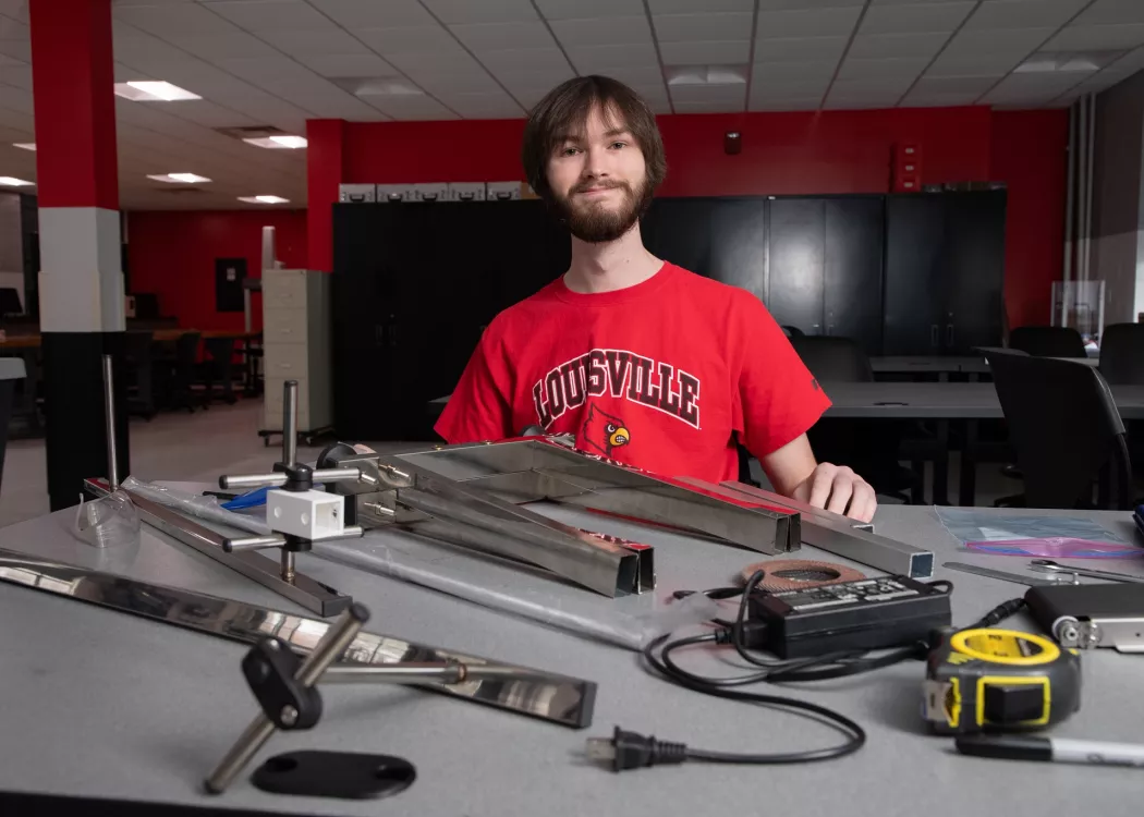 Young man smiling at worktable with metal and electrical parts