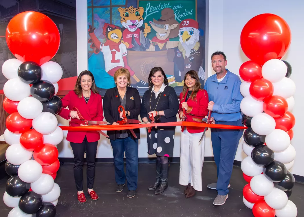 Five people cutting a red ribbon in front of character mural