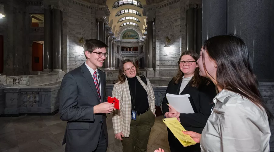 three young women and one young man all dressed professionally gather in a hallway in a government building