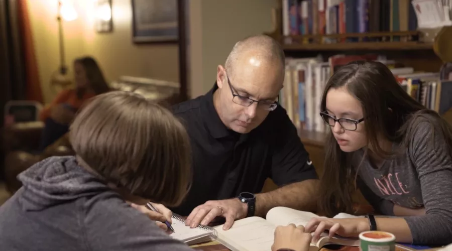 a man is studying at his home with two chilkdren sitting with him at a table