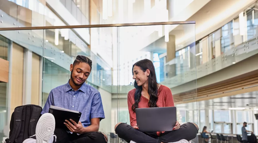 Two students are sitting on the floor while they study and do academic research on the second floor of the Belknap Academic Building.