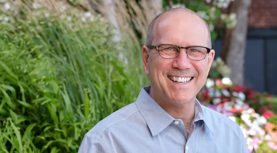 Head shot of a man standing in front of greenery