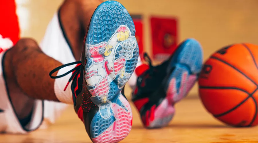 UofL Athletics Louie shoes close up with an image of Louie dunking a basketball. Basketball player wearing the shoes is sitting in the background with a basketball propped against their feet.