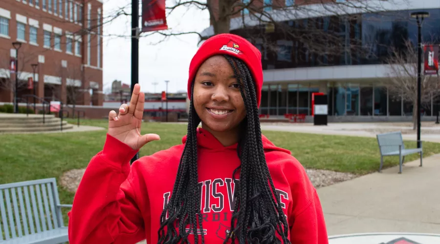 Woman wearing red UofL sweatshirt holding up a "L" sign