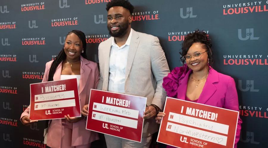 Three medical students hold signs indicating their residency placement.