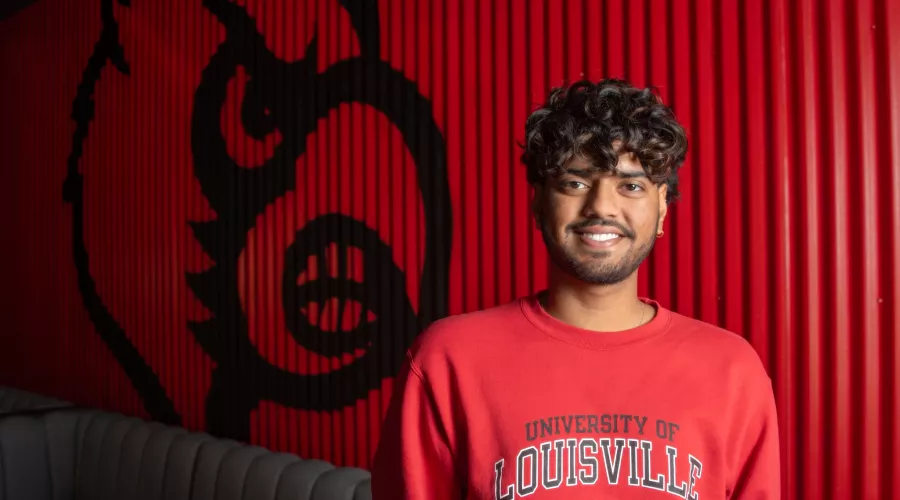 Student in red UofL sweatshirt with Cardinal bird on wall behind him.