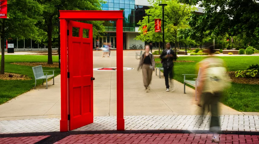 A red doorway on campus with students and an academic building