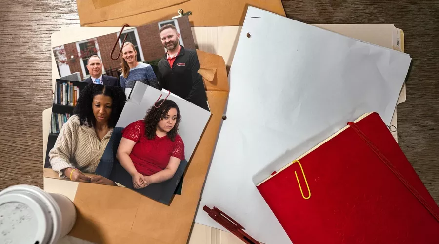 A red notebook and red pen on a desk with folders and photographs.