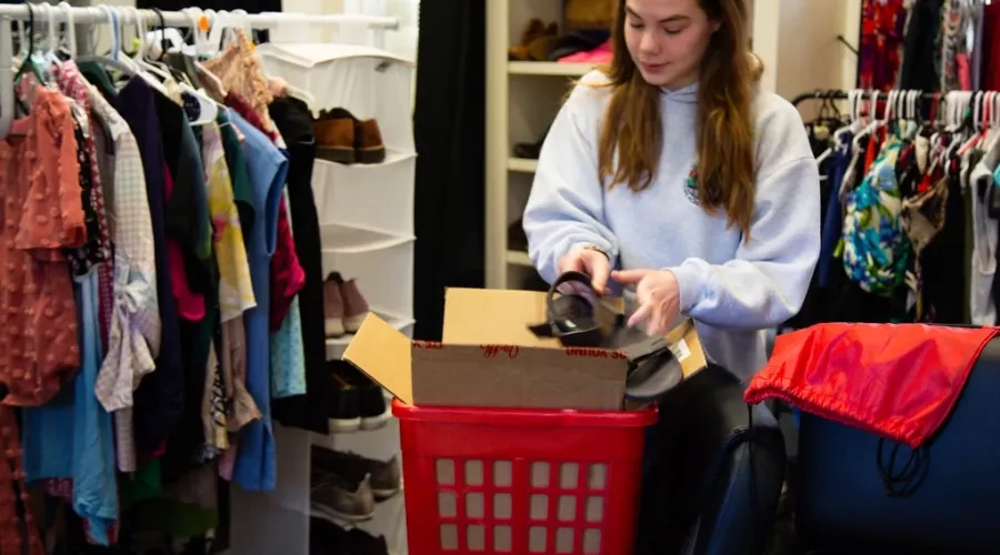 A person puts a shoe in a box, they are surrounded by clothing racks.