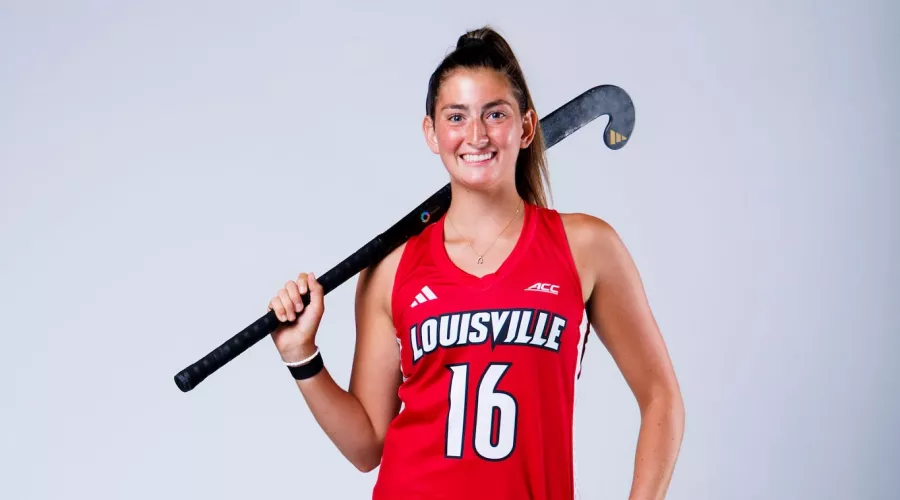 A portrait of UofL field hockey player Izzy Bianco in uniform holding a field hockey stick.