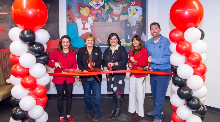 Five people cutting a red ribbon in front of character mural
