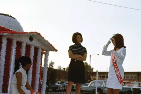 A color photo of three women standing atop a UofL Homecoming parade float in 1968.