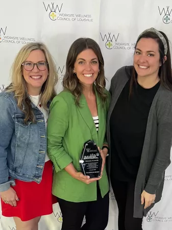 Three women together holding an award.