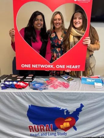 Three young women pose in a heart frame at a rural Kentucky health fair
