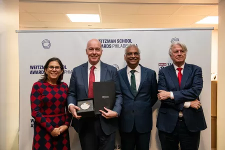Four people in business attire standing. One holds a folder and plaque.